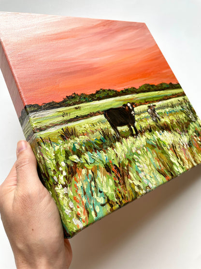 Hand holding a small painting of a landscape with cows.