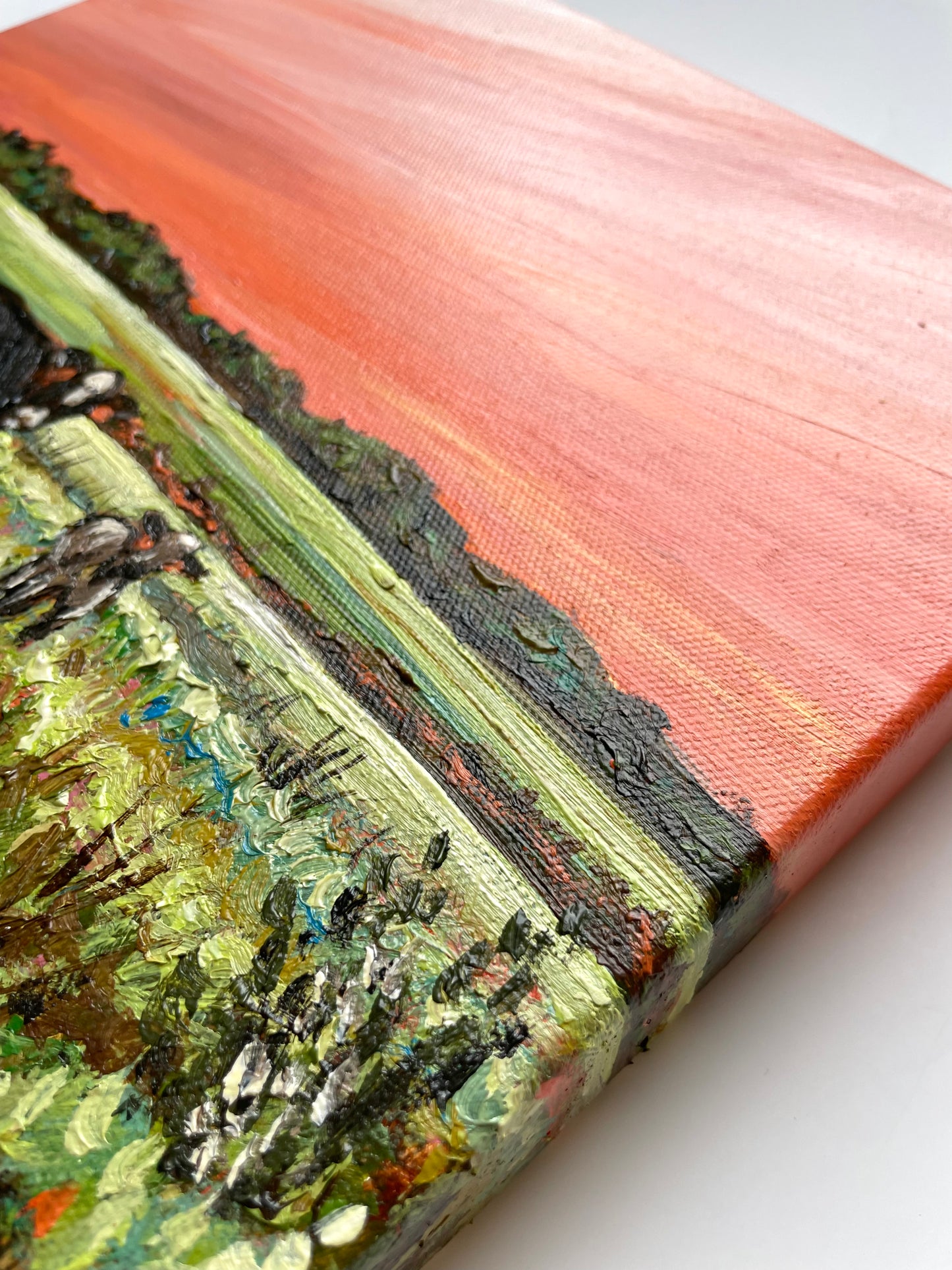 Close-up of a textured painting with earthy tones and an orange sunset sky 
