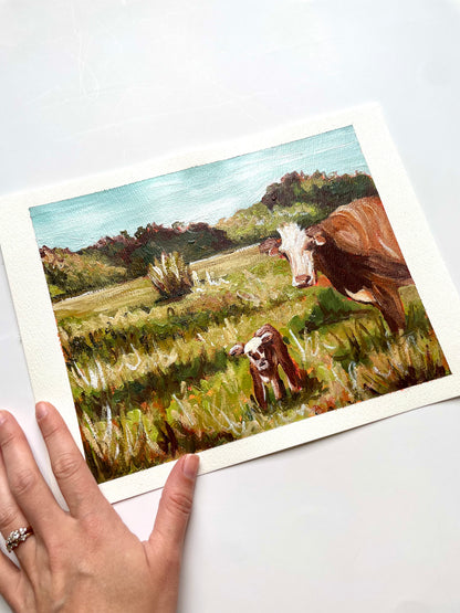 Mama and Baby Cow in a tall grassy field with warm brown colors and bright blue sky on a summer day. Painted on white paper. size 8x10